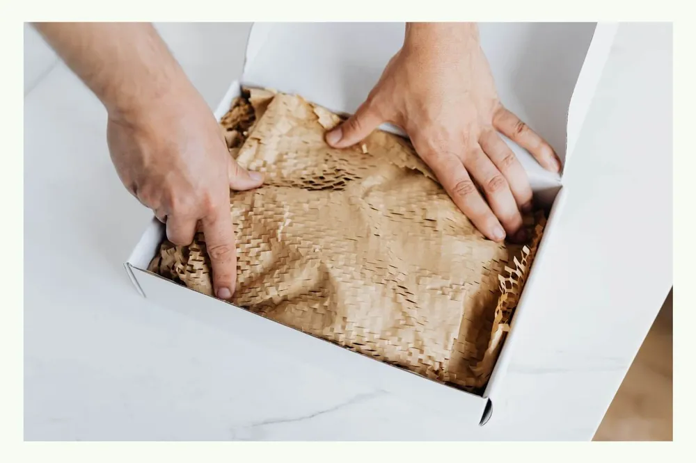 Hands placing paper padding into an open shipping box Hands placing paper padding into an open shipping box